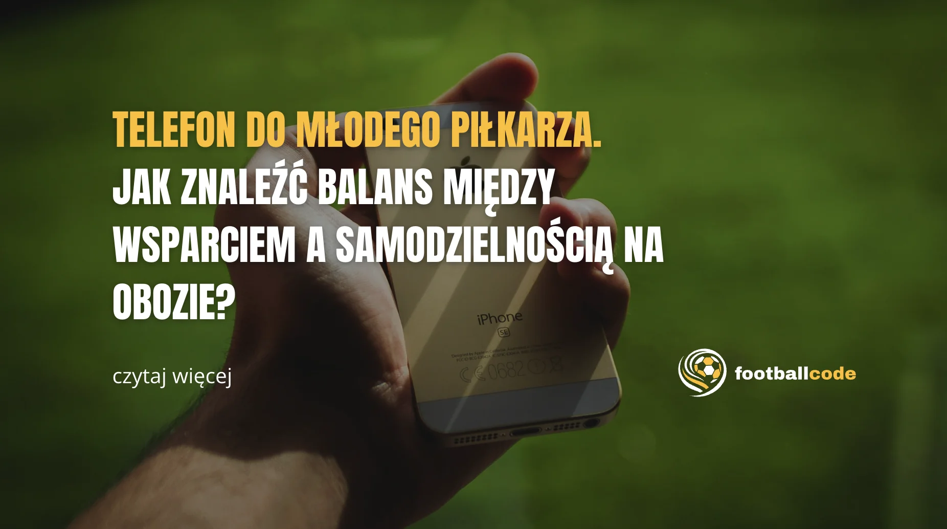 młody piłkarz siedzący na murawie z telefonem w dłoni